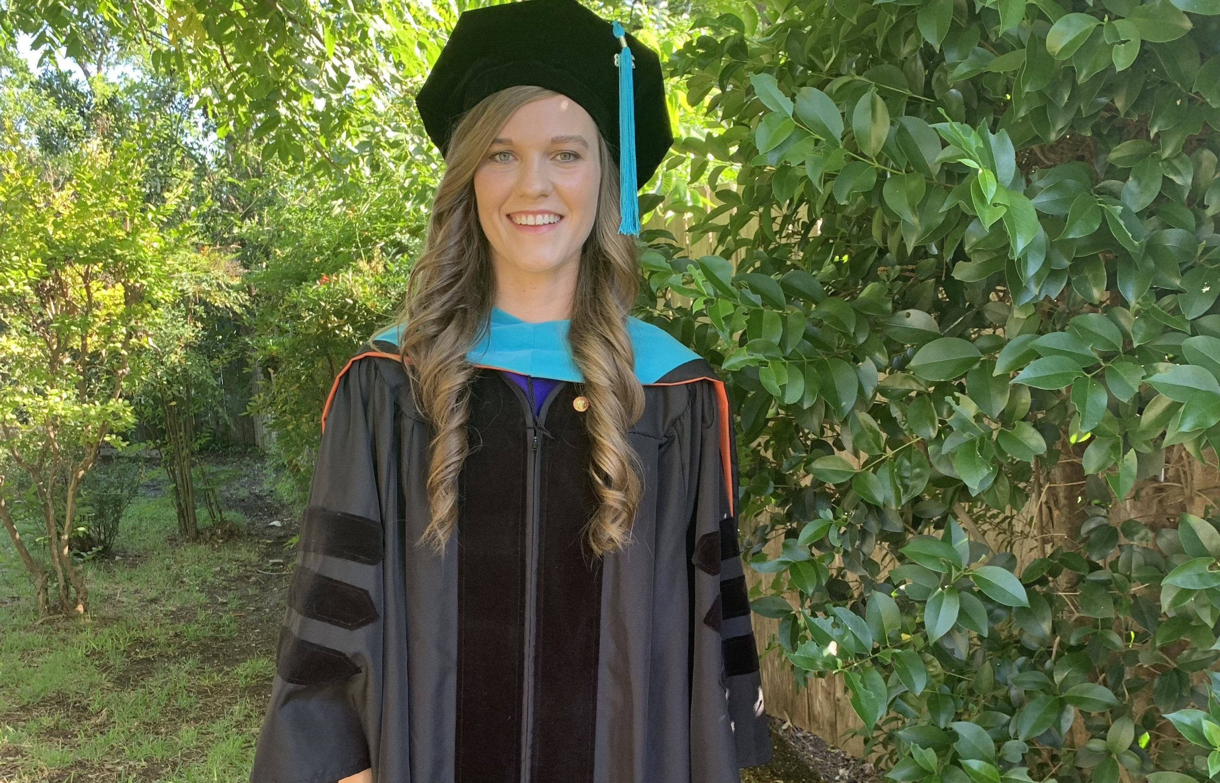 Brianna Halford in cap and gown with bushes in background