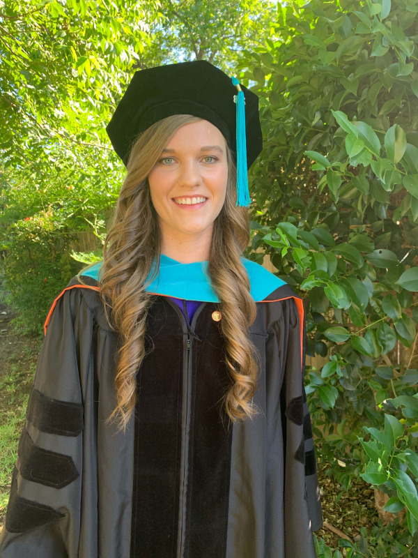 Brianna Halford in her cap and gown with bushes in the backgroun